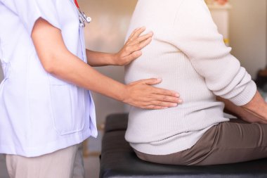 Physiotherapist doing treatment to senior woman patient in clinic ,Elderly women suffering from low-back lumbar pain,Physical therapy concept clipart