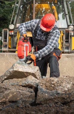 Güçlendirilmiş beton kaldırımı delmek için matkap kullanan bir işçi.