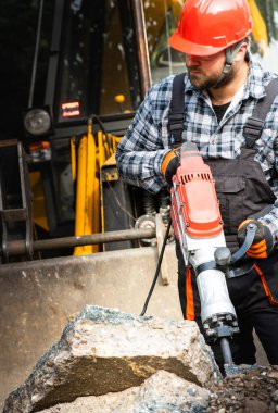 Güçlendirilmiş beton kaldırımı delmek için matkap kullanan bir işçi.