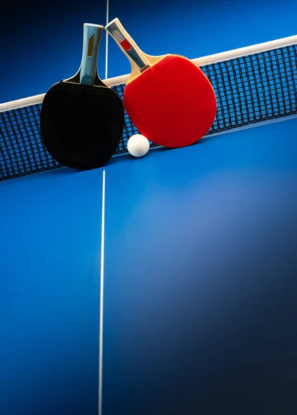 两个乒乓球球拍和一个蓝色桌子上的球网 — 图库照片