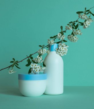 Kozmetik ürünleri için bir şişe ve etiketsiz bir kavanoz krema. Üstünde çiçekler olan bir dal. Yüz bakımı konsepti.