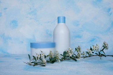 Mavi ve beyaz arka planda güzellik hijyeni için çeşitli konteynırların toplanması. Tuval. Yukarıdan çiçekli bir dal