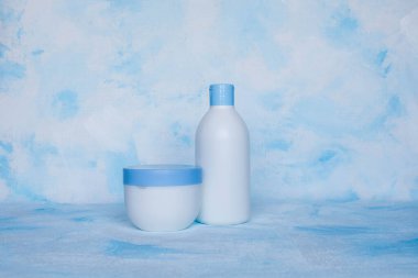 Mavi ve beyaz arka planda güzellik hijyeni için çeşitli konteynırların toplanması. Tuval. Yukarıdan çiçekli bir dal