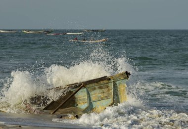 Batı Afrika. Moritanya 'da. Deniz suyu, Nouakchott şehrinin yakınlarındaki Atlantik Okyanusu 'nda kıyıya vuran kırık bir balıkçı teknesinin kalıntılarının üzerindeki kıyı dalgalarının etkisinden fışkırıyor..
