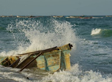 Batı Afrika. Moritanya 'da. Deniz suyu, Nouakchott şehrinin yakınlarındaki Atlantik Okyanusu 'nda kıyıya vuran kırık bir balıkçı teknesinin kalıntılarının üzerindeki kıyı dalgalarının etkisinden fışkırıyor..