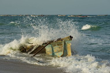Batı Afrika. Moritanya 'da. Deniz suyu, Nouakchott şehrinin yakınlarındaki Atlantik Okyanusu 'nda kıyıya vuran kırık bir balıkçı teknesinin kalıntılarının üzerindeki kıyı dalgalarının etkisinden fışkırıyor..