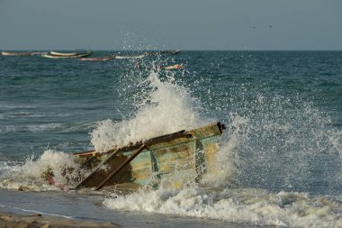 Batı Afrika. Moritanya 'da. Deniz suyu, Nouakchott şehrinin yakınlarındaki Atlantik Okyanusu 'nda kıyıya vuran kırık bir balıkçı teknesinin kalıntılarının üzerindeki kıyı dalgalarının etkisinden fışkırıyor..