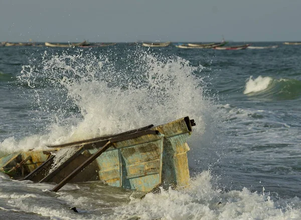 Batı Afrika. Moritanya 'da. Deniz suyu, Nouakchott şehrinin yakınlarındaki Atlantik Okyanusu 'nda kıyıya vuran kırık bir balıkçı teknesinin kalıntılarının üzerindeki kıyı dalgalarının etkisinden fışkırıyor..