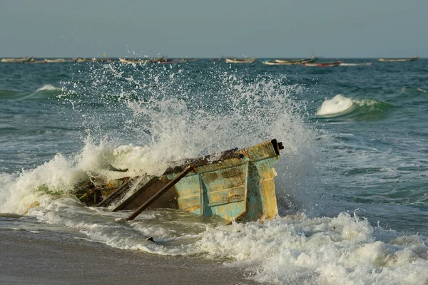 Batı Afrika. Moritanya 'da. Deniz suyu, Nouakchott şehrinin yakınlarındaki Atlantik Okyanusu 'nda kıyıya vuran kırık bir balıkçı teknesinin kalıntılarının üzerindeki kıyı dalgalarının etkisinden fışkırıyor..