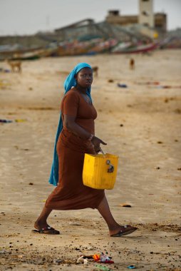 Saint-Louis 'de. Senegal. 10 Ekim 2021. Siyah bir köy kızı Atlantik Okyanusu kıyısında plastik bir kova çöp taşıyor. Okyanuslar bu yüzden tıkanır..