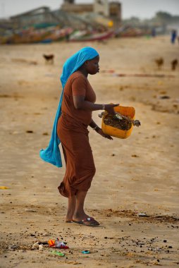 Saint-Louis 'de. Senegal. 10 Ekim 2021. Siyah bir köy kızı Atlantik Okyanusu kıyısında plastik bir kova çöp taşıyor. Okyanuslar bu yüzden tıkanır..