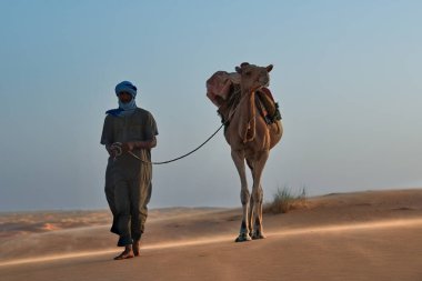 Shingetti. Moritanya 'da. Ekim 05, 2021. Ulusal elbiseli yalnız bir Mağripli Sahra Çölü 'nün kumlu kumullarında tek hörgüçlü bir deveye önderlik ediyor..