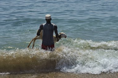 Dakar. Senegal. 12 Ekim 2021. Bir balıkçı köyünün koyu tenli sakini Atlantik Okyanusu 'nun Afrika kıyılarında yıkanmak ve temizlenmek için bir koyun taşıyor..