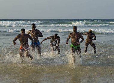 Dakar. Senegal. 13 Ekim 2021. Kaslı güreşçiler, Laamb güreş müsabakasının bitiminden sonra deniz kenarından kumlu sahile doğru bol bol su püskürterek koşuyorlar..