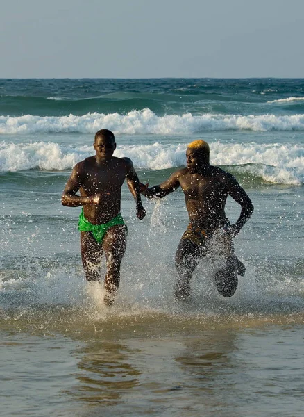 Dakar. Senegal. 13 Ekim 2021. Kaslı güreşçiler, Laamb güreş müsabakasının bitiminden sonra deniz kenarından kumlu sahile doğru bol bol su püskürterek koşuyorlar..
