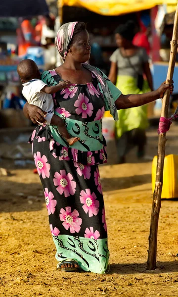 Saint-Louis. Senegal. October 11, 2021. A girl in a colorful national dress with a baby in her arms poses thoughtfully near the huts and buildings of a fishing village.