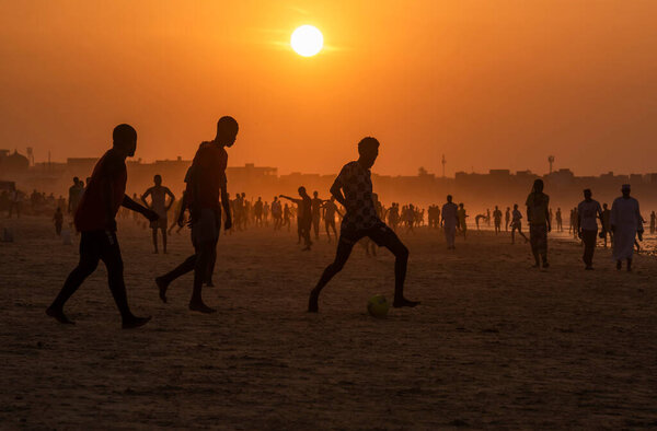 Dakar. Senegal. October 13, 2021. Young residents of the African capital on the city beach massively play beach soccer in the glare of the blazing sunset sun.