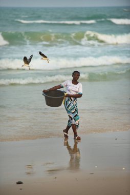 Saint-Louis 'de. Senegal. 10 Ekim 2021. Balıkçı köyünden genç bir kız okyanusta yıkanmış siyah plastik bir leğen taşıyor..