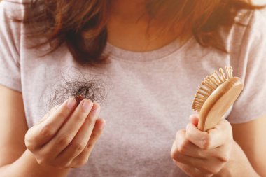 Genç bir kadın, elinde tarakla saç dökülmesinden endişeleniyor. Hormonal dengesizlik, stres konsepti. Sağlık hizmeti kavramı