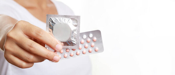 Contraceptive means: Woman hand holding contraceptive pills and condom sitting on sofa background. Protection, safe sex. Contraception, concept birth control. Copy space