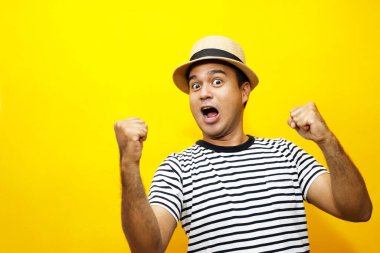 Sıradan giyinmiş neşeli Asyalı bir adamın portresi. Gülümseyen bir şapka takıyor ve kameraya başarıyla başparmak kaldırıyor. sarı arkaplan üzerinde izole. 