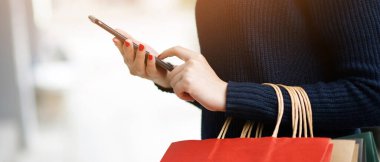 Moda mağazasında alışveriş yapmak için bir sürü alışveriş çantası tutan bir iş kadını. Müşteriler internet üzerinden alışveriş yapmak için cep telefonu kullanabilirler. Satın alma ve ödeme havalesi için..