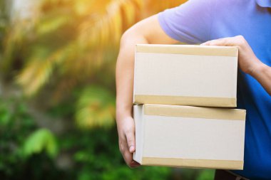 Paket teslimatçısı koruyucu eldiven takıyor mavi ve maske takıyor. Hijyen mikrobu ve bakterileri korumak için eve gönderilen bir servis vasıtasıyla. El ele tutuşmalar ve teslim olma müşterileri bir kutu kabul ediyor