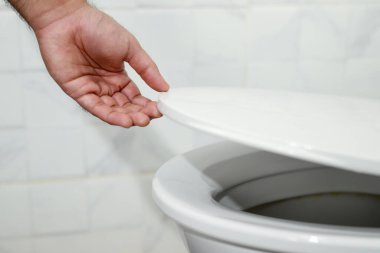 Adamın eli tuvalet kapağını açıyor.