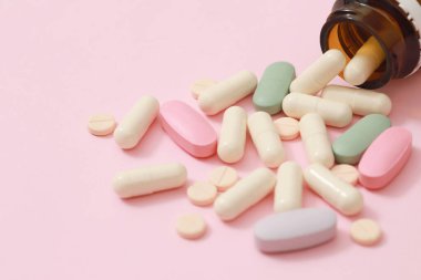 İlaç şişesi dökülüyor. Renkli haplar, pembe arka plandaki tabletlere konuyor. İlaç tıbbi sağlık eczanesi konsepti. İlaç olarak kullanılan antibiyotik hapları su toplayan paketlerde..  