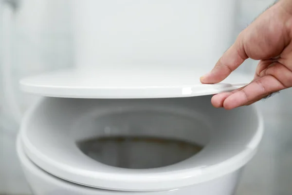 man\'s hand opening the toilet lid