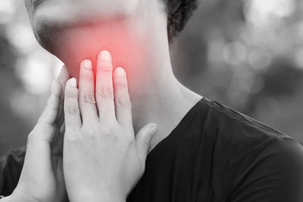 sore throat pain. Closeup of young man sick holding her inflamed throat using hands to touch the ill neck in blue shirt on gray background. Medical and healthcare concept. Focus red on to show pain.