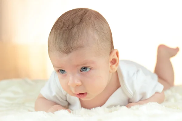 Adorable baby boy in a white t-shirt lies on his stomach — Stock Photo, Image
