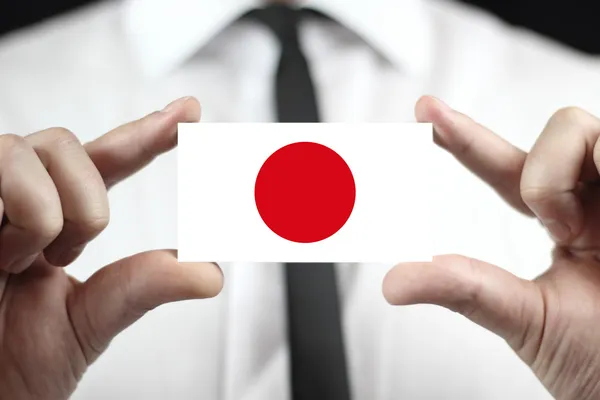 Empresário segurando um cartão de visita com uma bandeira do Japão — Fotografia de Stock