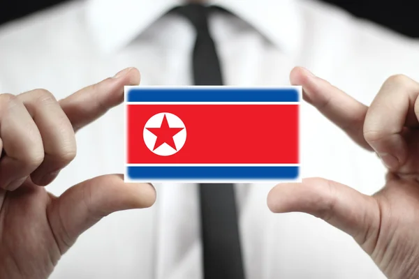 Empresário segurando um cartão de visita com uma bandeira da Coreia do Norte — Fotografia de Stock