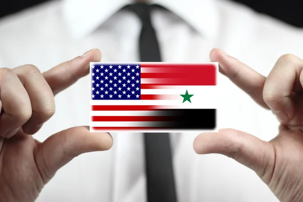 Uomo d'affari in possesso di un biglietto da visita con bandiera USA e Siria — Foto Stock