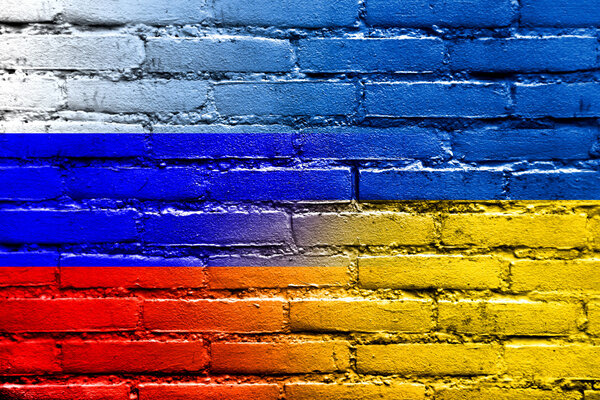 Флаг Украины и России раскрашен на кирпичной стене
