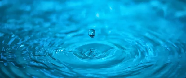 Una gota de agua azul de primer plano cae sobre el remolino del embudo de agua. Contexto —  Fotos de Stock