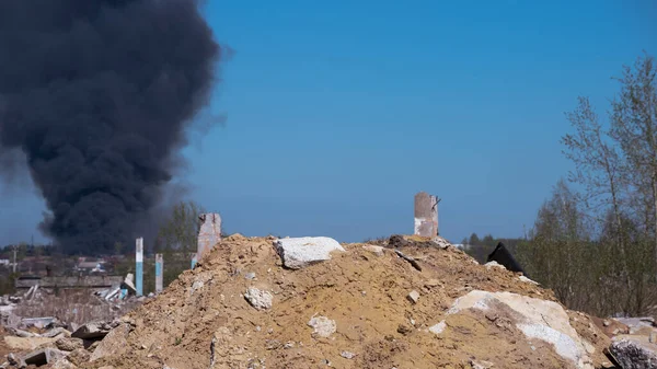 Los restos de hormigón de un edificio en ruinas con zancos sobresalientes sobre un fondo de humo negro contra un cielo azul. Contexto —  Fotos de Stock