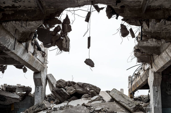 Бетонные фрагменты на металлической арматуре с остатками здания против серого неба. Фон.