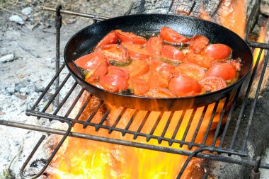 Domatesler, çırpılmış yumurta hazırlamak için, metal bir ızgarada, siyah bir tavada kızartılır..