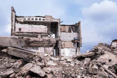 Önünde beton moloz yığını olan gri bulutlu mavi gökyüzüne karşı yıkılmış bir bina. Arkaplan.