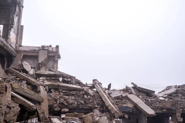 Ruínas de fragmentos de concreto de um edifício destruído em uma névoa nebulosa contra um céu cinza. Contexto — Fotografia de Stock