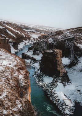 Kışın Fjadrargljufur Kanyonu ve Fjadra Nehri 'nin hava aracı manzarası. Beyaz kar ve mavi nehir. İzlanda, Reykjavik yakınlarında. Fotoğraf İzlanda 'da çekildi.