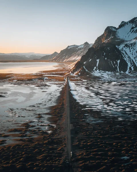 Panorama aérien de drone de route de gravier au coucher du soleil avec la montagne Vestrahorn et la plage de stokksnes en Islande en arrière-plan. Paysages hivernaux avec neige et soleil. — Photo