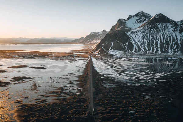 해 가 지는 곳에 자갈길로 이어지는 공중 드론 파노라마와 베스티 라 혼 산, 아이슬란드 해변 이 배경으로 펼쳐져 있다. 눈 과 태양 이 있는 겨울 풍경. — 스톡 사진
