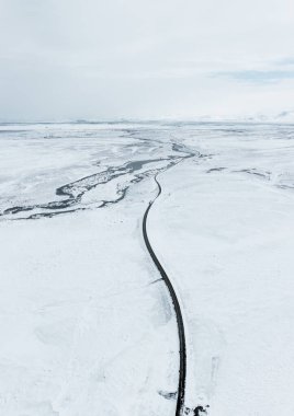 Hava aracı kışın İzlanda 'da yokuş yukarı manzaralı. Asfalt yolu, yanlamasına karla kaplı kış boyunca mavi gökyüzü.