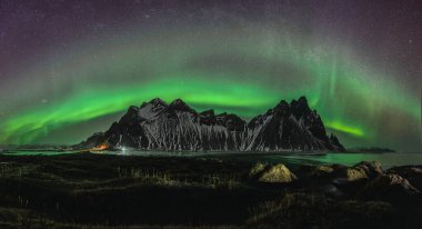 Vestrahorn Stockknes sıradağları. Aurora Borealis ve İzlanda sahillerinde yansıması var. İzlanda 'nın en ünlü doğa mirasından biri..