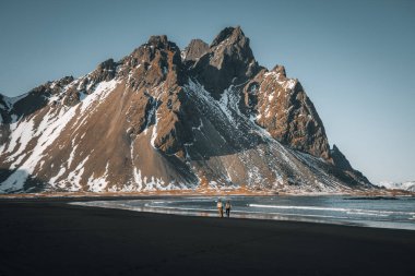 Gün batımında sahilde duran genç turist ve İzlanda 'daki Stoksnes Burnu' ndaki Vestrahorn Dağı 'nın muhteşem yansıması. Güzel kar kaplı dağlar. Konum: Stoksnes pelerini