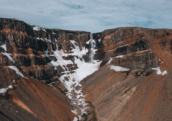 Letecký dron záběr Hengifossova vodopádu na východě Islandu s trochou sněhu a modré oblohy. — Stock fotografie