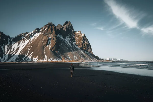 Ung man turist står på stranden under solnedgången runrise och vacker reflektion av Vestrahorn berg på Stokksnes udde på Island. Vackra snötäckta berg. Plats: Stokksnes udde — Stockfoto